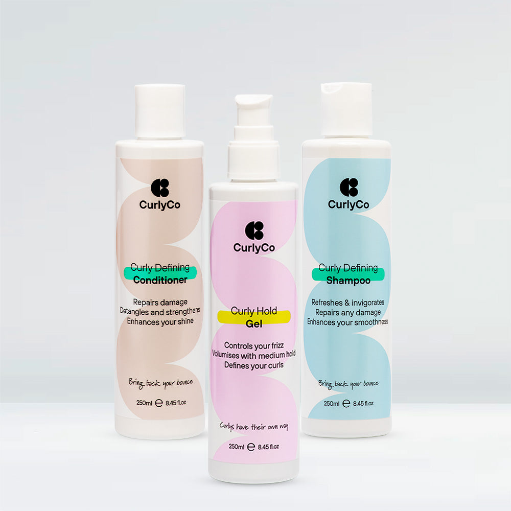 Four curly hair care products from CurlyCo, including shampoo, conditioner, cream, and mousse.